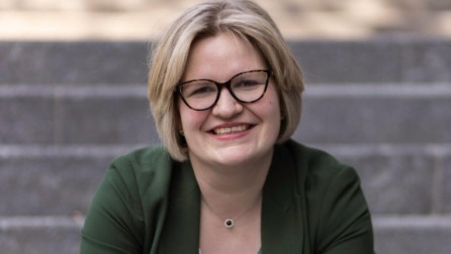 Foto van Ike Lieshout, zittend op een trap in een groen pak. Ze heeft blond, kort haar en een bril op.
